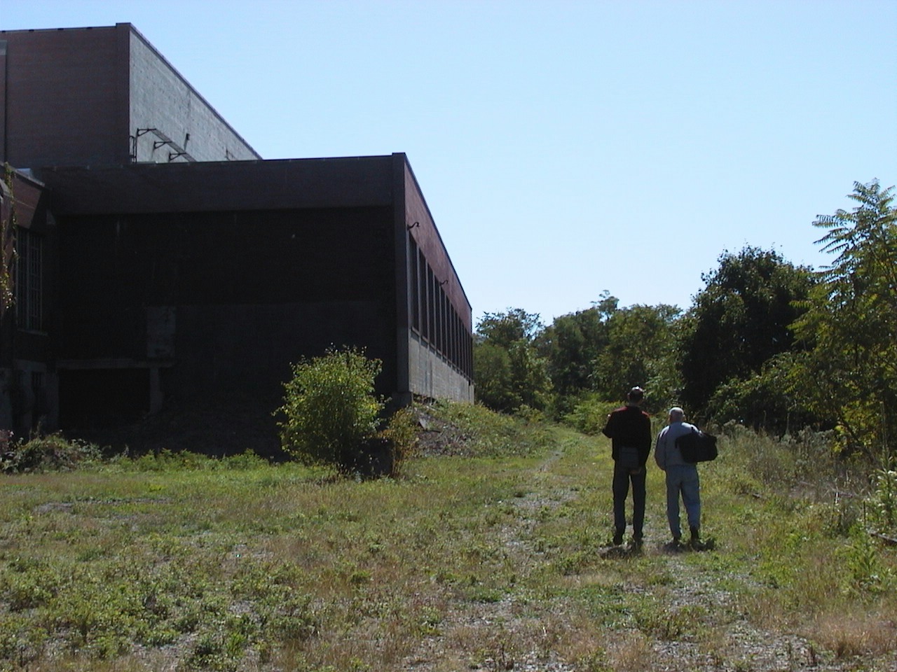 Photo of two men walking away with a large factory building to the left