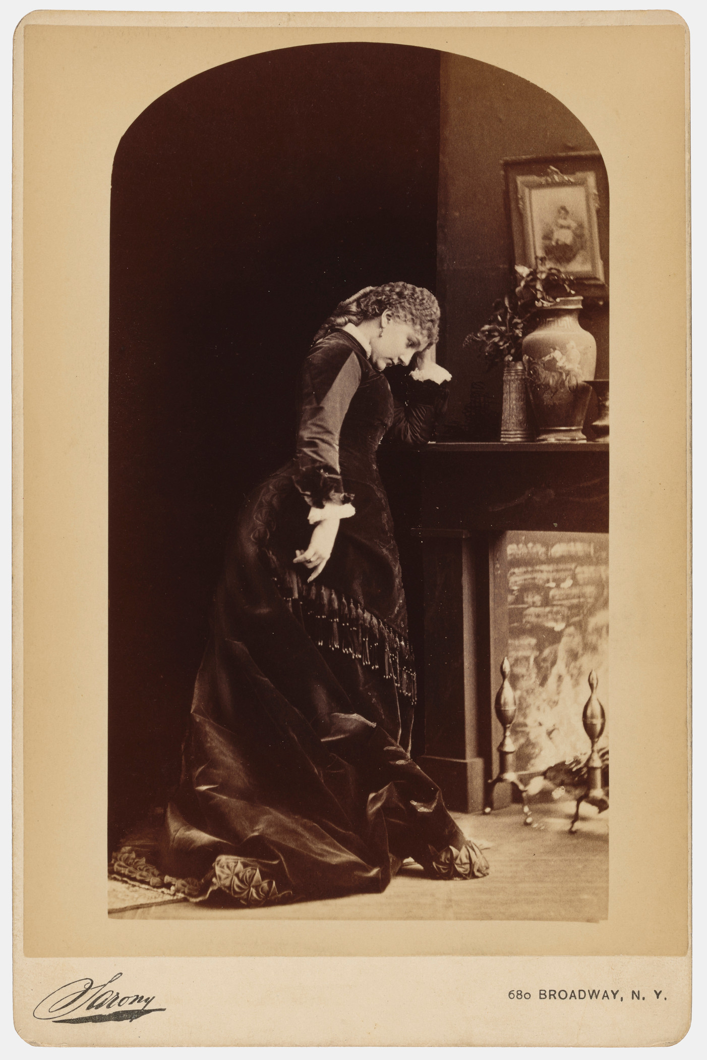Woman wearing 19th century dress resting head in hand by a decorated mantle