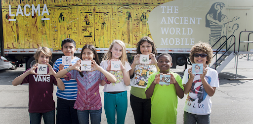 Students show their art projects while standing in front of the Ancient World Mobile.