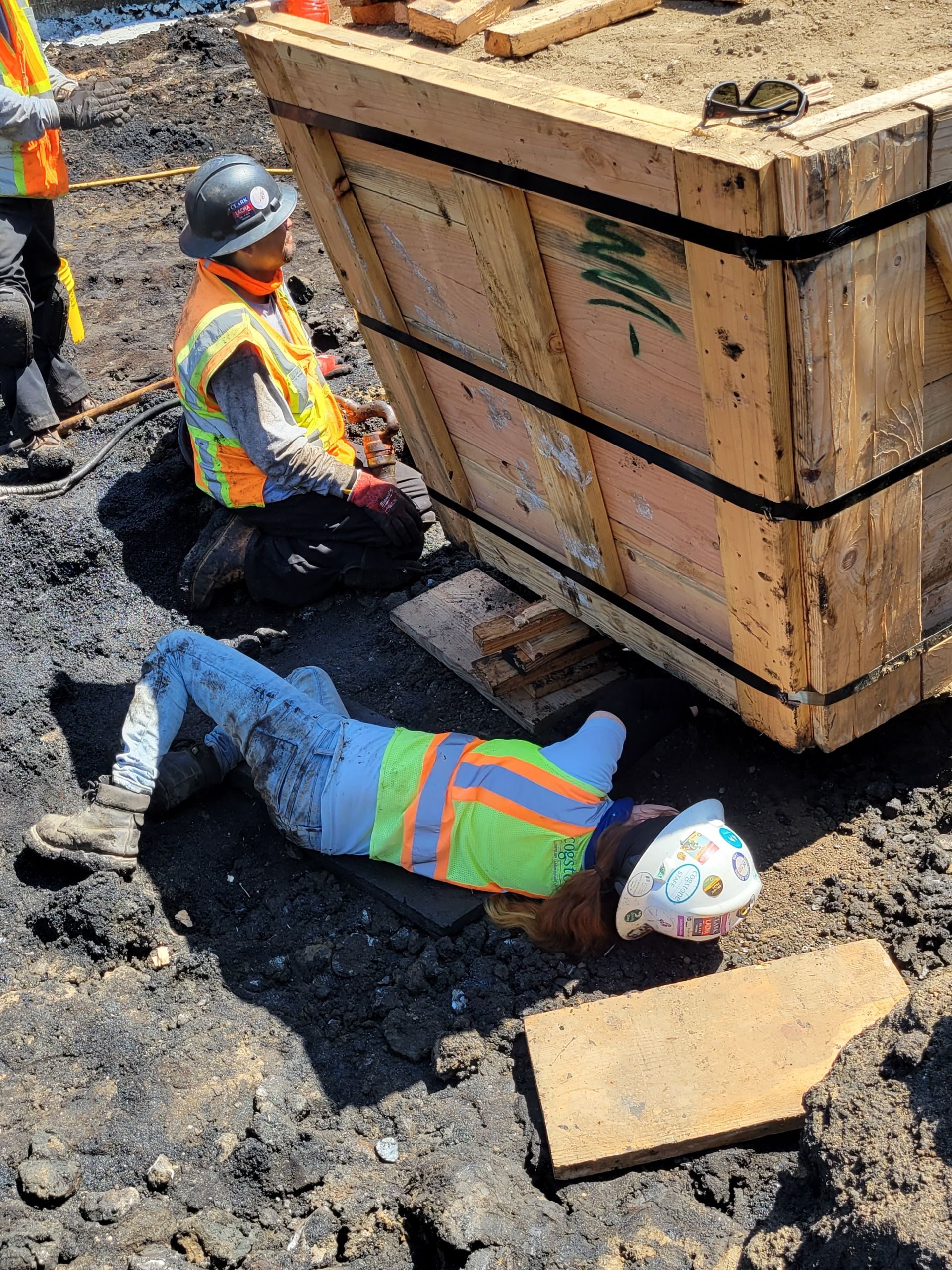 a person lying on ground reaching under box in construction site