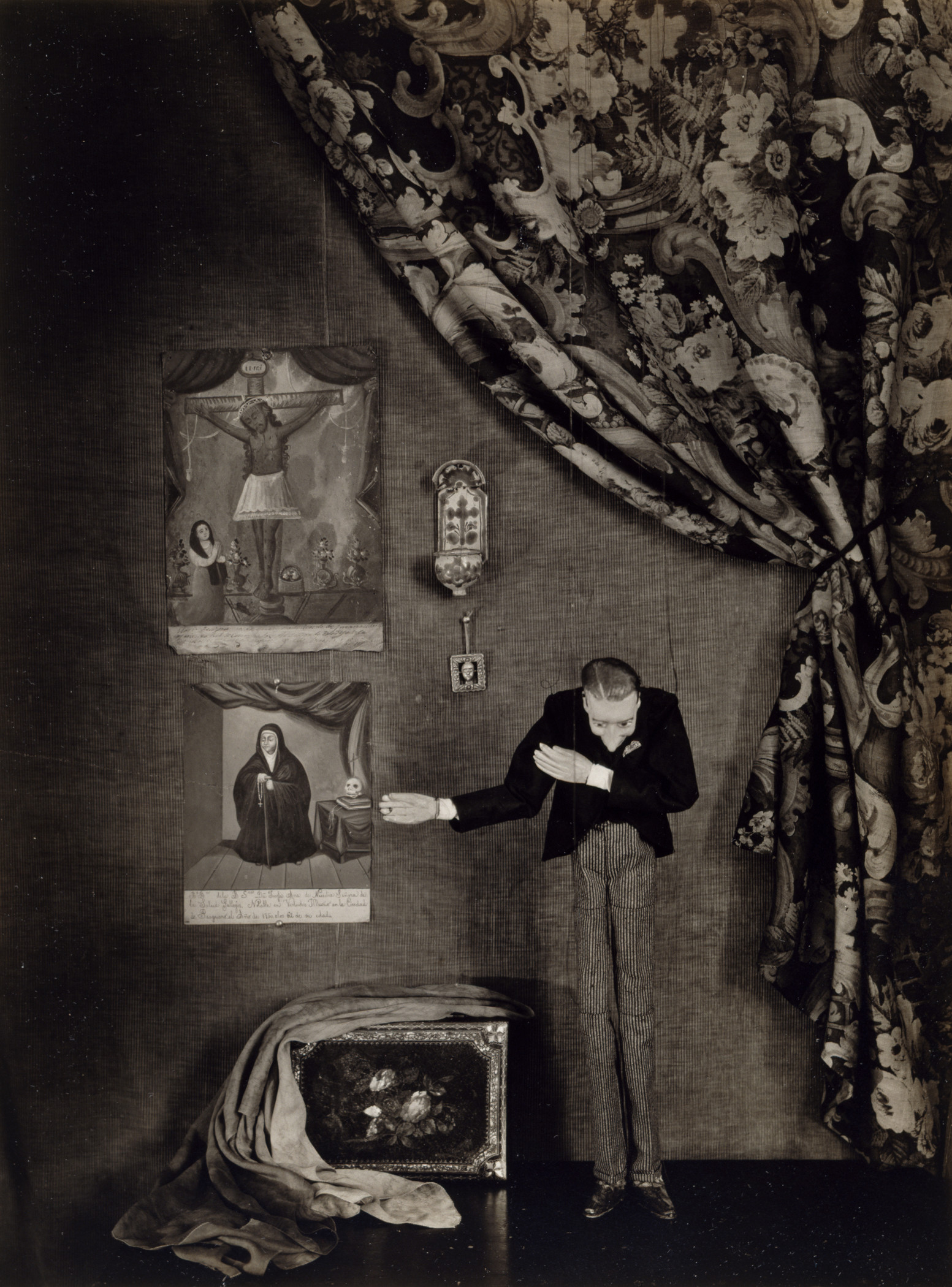 A black and white photograph with a marionette in a suit bowing, next to artworks