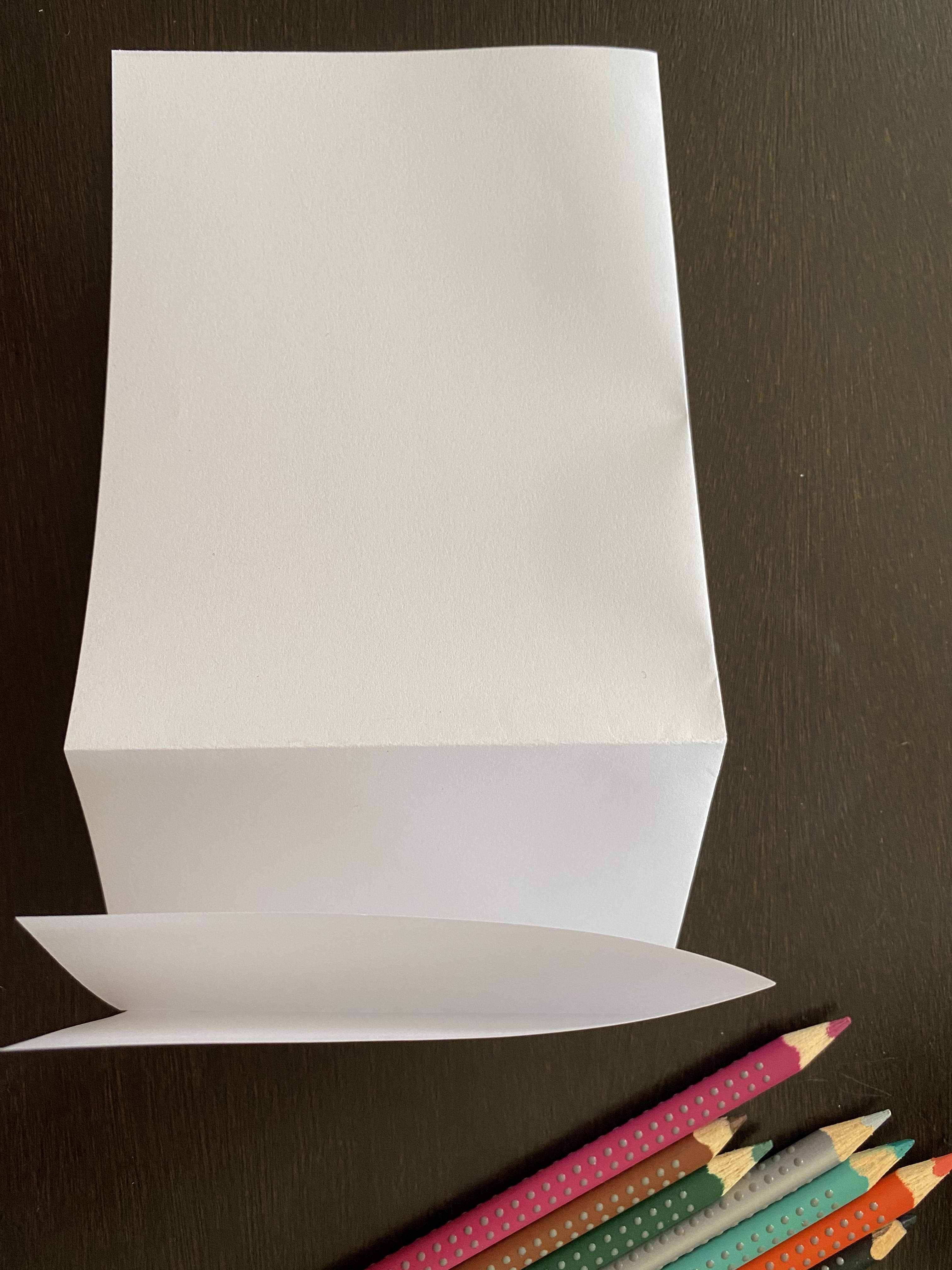 Long rectangle of white paper being folded with colored pencils on the side