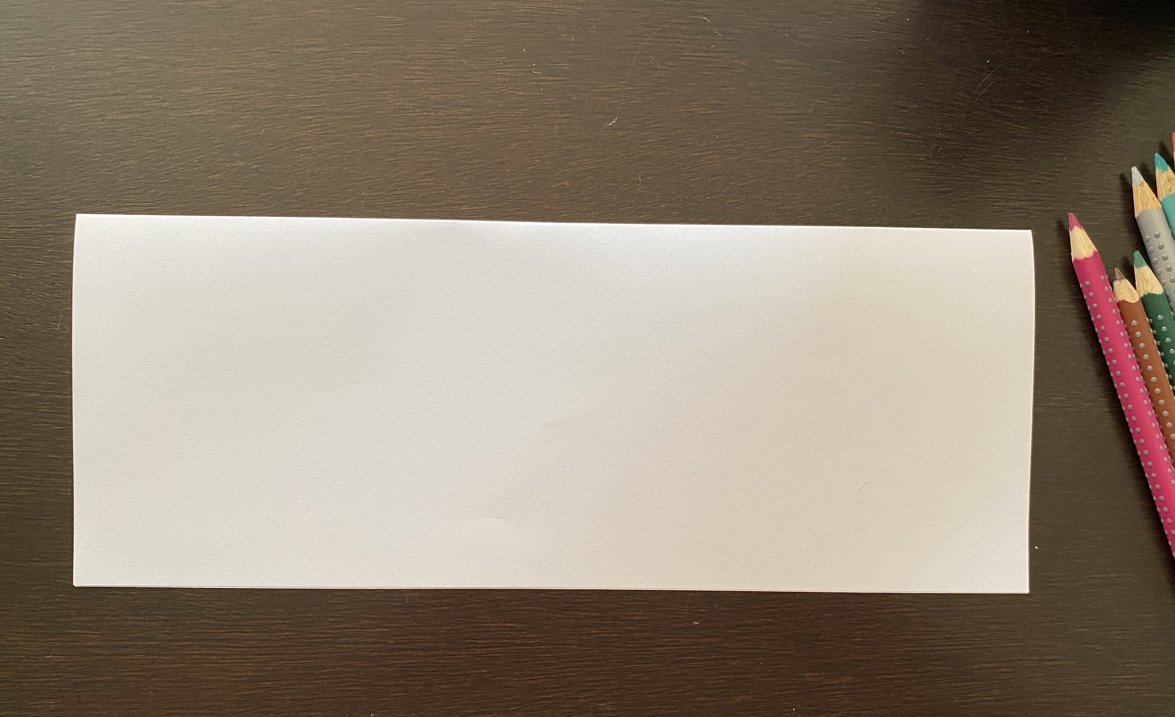 Long rectangle of white paper with colored pencils on the side