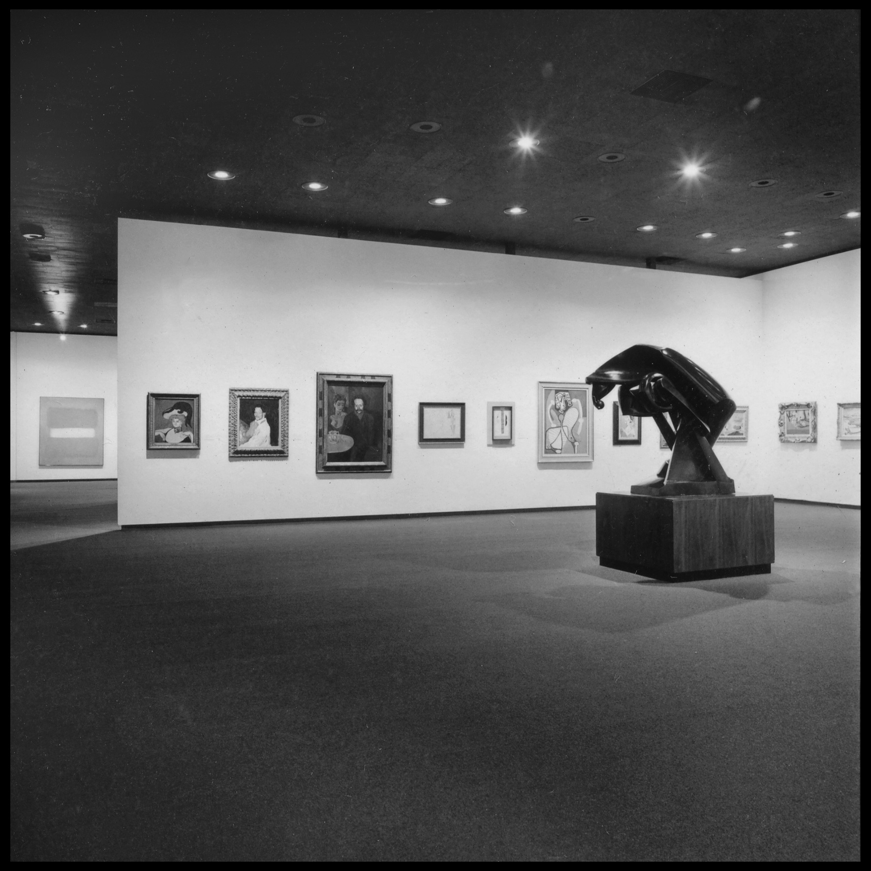 Black and white photograph of gallery with paintings and a sculpture