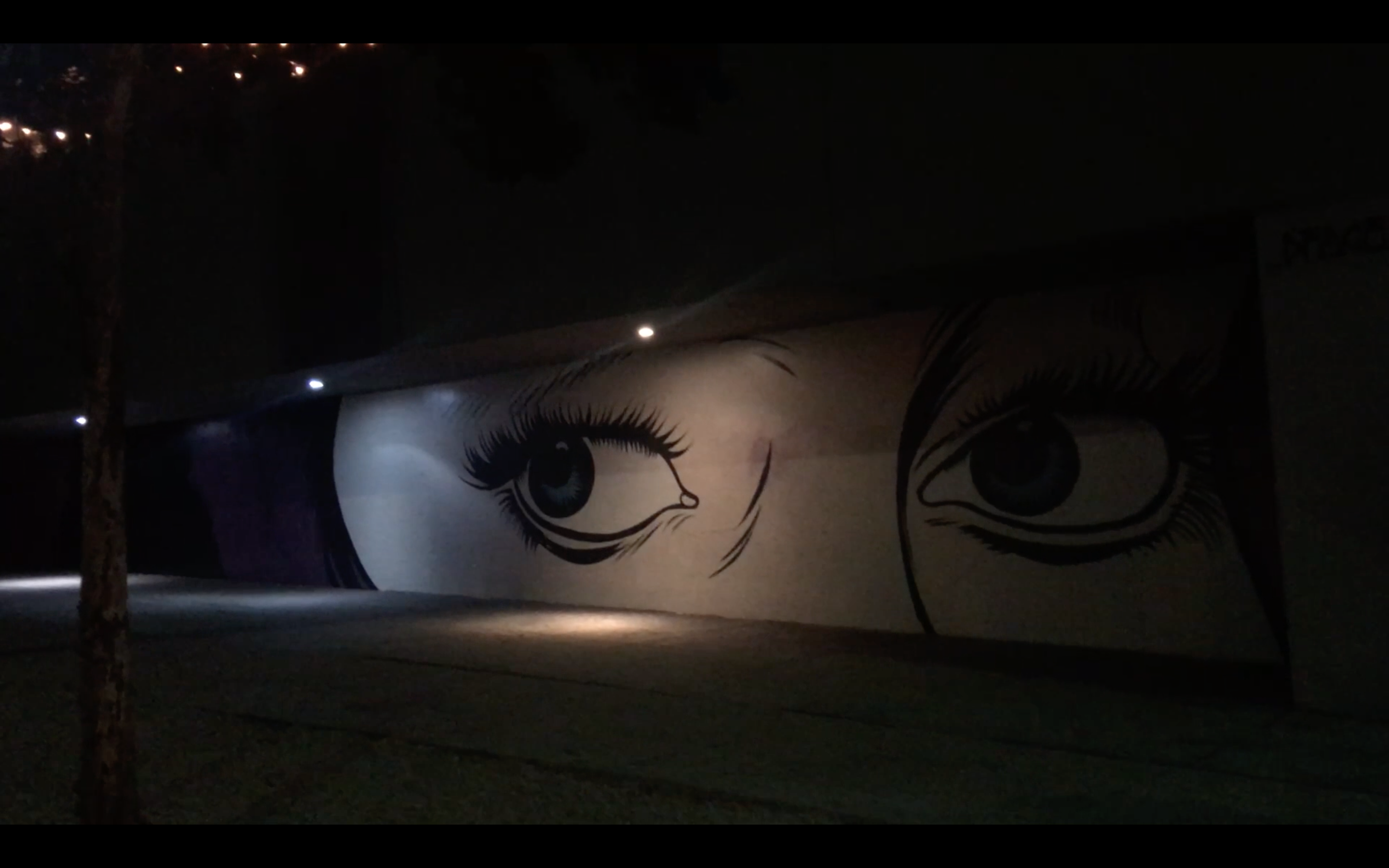 mural of eyes painted on wall, viewed under streetlights, nighttime