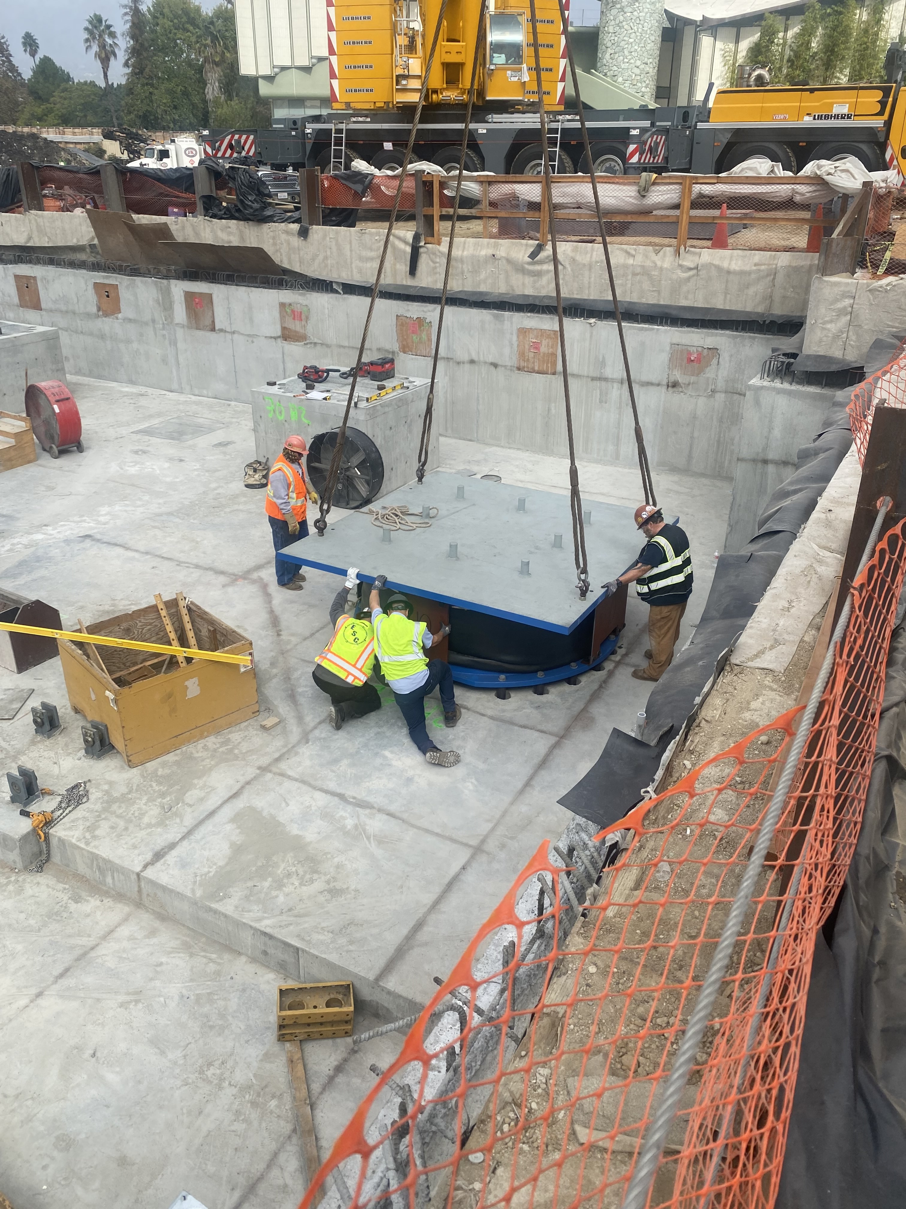 Four workers actively placing a large isolator in place on a construction site