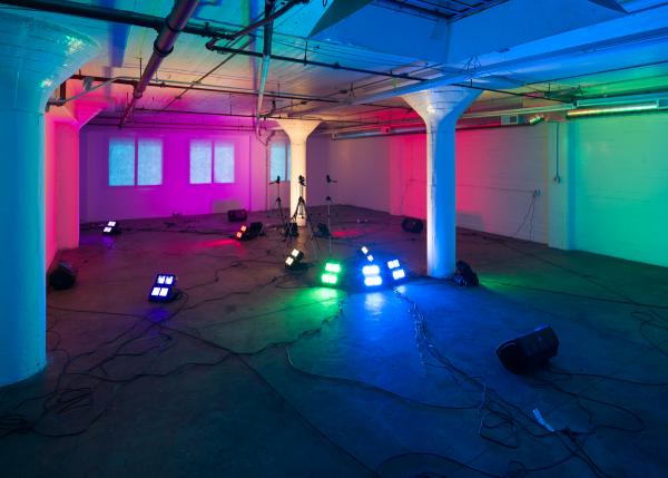 Diana Thater's installation Yes, there will be singing—an image of an open, warehouse-type interior with colored lights illuminating the room