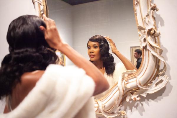 Woman wearing fur shawl fixing her hair in mirror during Dapper Day event in 2019