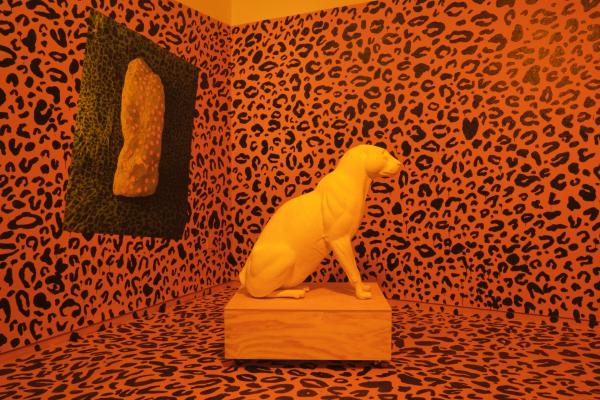 installation of room with orange and black leopard print walls and floor with a white leopard statue in the center