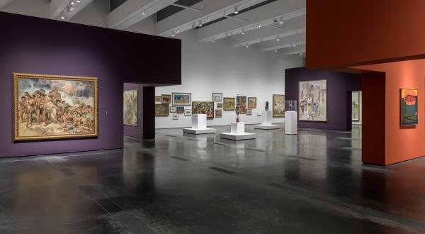 Gallery view with art on the walls that are painted purple, white, and maroon