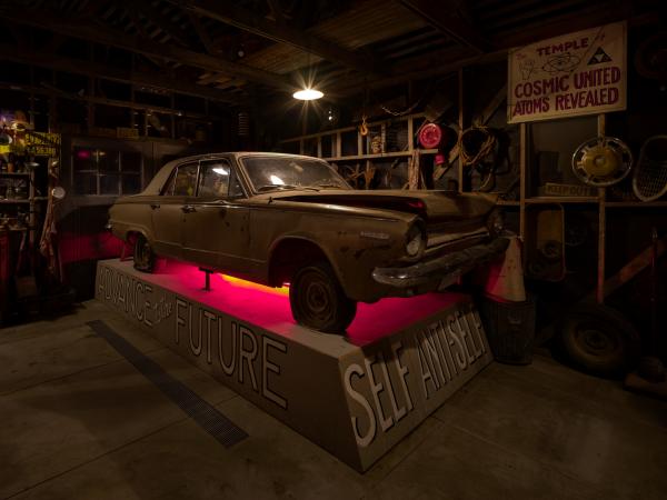 Installation of Michael C. McMillen's Central Meridian, a dark, workshop-like space featuring a vintage car