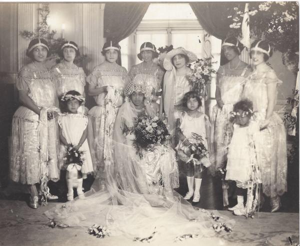 A group of women and three young girls in wedding finery and headpieces pose for a portrait