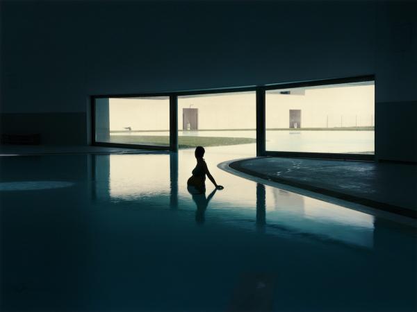 Pregnant woman standing in waist-deep indoor pool, lit in silhouette