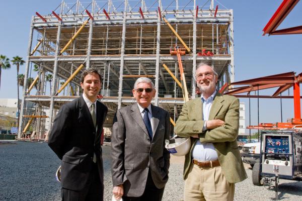Three men stand in front of a three story building under construction