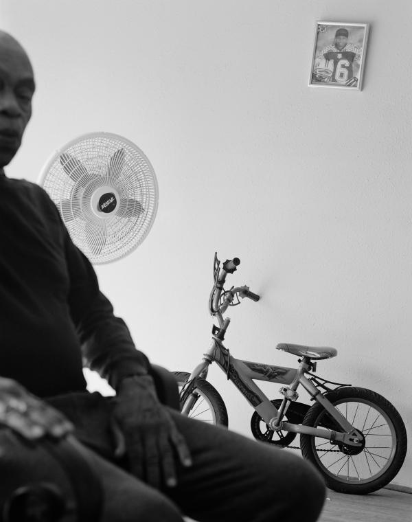 Black and white photo of man half out of frame with bicycle and standing fan in the background