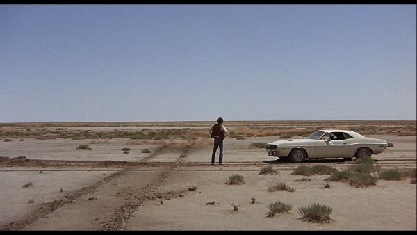 Man standing next to old car on desert road