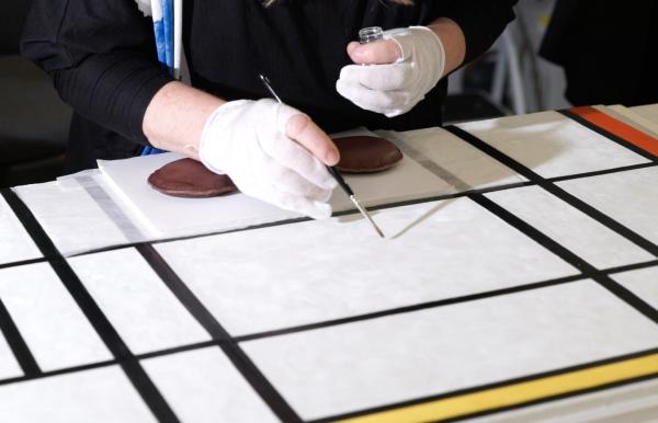 Close-up of white geometric painting being touched up with a brush by gloved hands