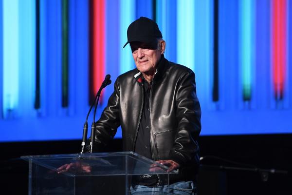 Man in black ball cap and leather jacket at podium