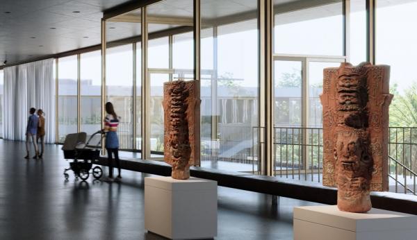 Two sculptures displayed in light-filled gallery with person with stroller