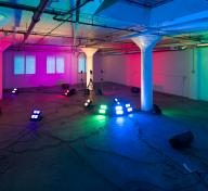 Diana Thater's installation Yes, there will be singing—an image of an open, warehouse-type interior with colored lights illuminating the room