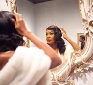 Woman wearing fur shawl fixing her hair in mirror during Dapper Day event in 2019