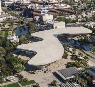 Overhead view of organically shaped gray building surrounded by vegetation and buildings