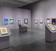 Gallery view with paintings on lavender walls and podiums