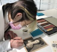 Conservation intern painting a black and white print of a woman