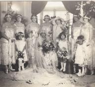 A group of women and three young girls in wedding finery and headpieces pose for a portrait