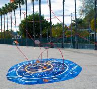 Blue portal on ground with red yarn emerging into the air with palm trees in background