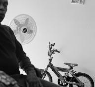 Black and white photo of man half out of frame with bicycle and standing fan in the background