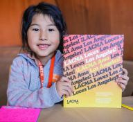 Photo of young girl holding a book that says "LACMA Loves Los Angeles!" on the cover