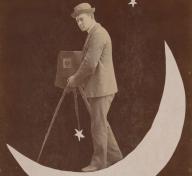 Black and white photo of a man on a cut-out moon with a camera and tripod