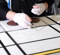 Close-up of white geometric painting being touched up with a brush by gloved hands