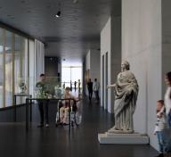 People viewing sculptures in a gallery with floor-to-ceiling windows on one side