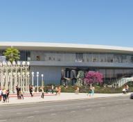 Rendering of gray building with art installation of streetlamps on the left, sculptures in the center, and visitors along the street