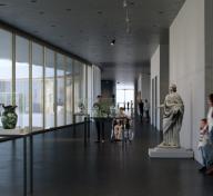 Rendering of interior of gallery with floor to ceiling windows on the left and visitors and artwork